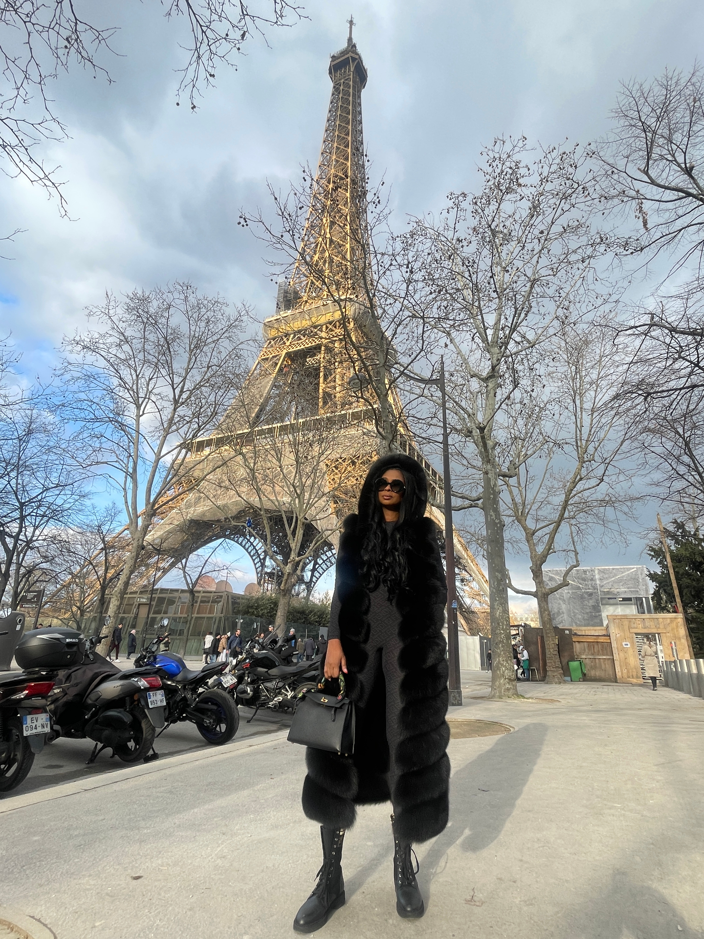 Jennifer Gold in a hooded fur coat in front of the Eiffel Tower in Paris.